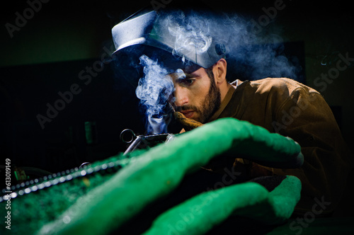 A man in a welding helmet inspects a smoking weld on a piece of metal and concrete sculpture