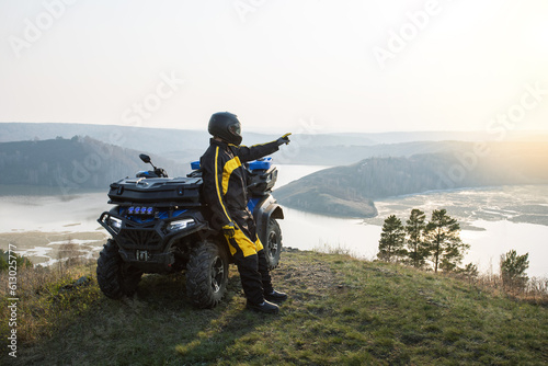 Fototapeta Naklejka Na Ścianę i Meble -  Man is watching the sunset from the mountain standing near ATV. Offroad travel adventure trip expedition.