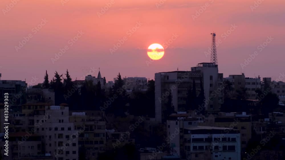 Time lapse of Amman capital city in Jordan, sun dipping behind urban cityscape view with beautiful pink sky at sunset Time lapse of Amman capital city in Jordan, sun dipping behind urban cityscape view with beautiful pink sky at sunset