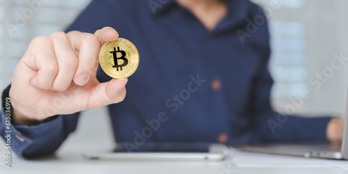 Bitcoin Cryptocurrency investment concept. Trader or investor hand holds Bitcoin Cryptocurrency gold coins. Businessman shows Bitcoin Cryptocurrency on hands while using laptop for trading. Banner.