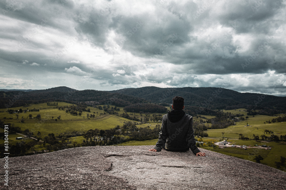 landscape photography , Solitary figure on cliff's edge, amid rugged rocks, under an expansive, cloud-filled sky, evoking adventure, courage, and awe at nature's grandeur, nature photo, adventure, Man