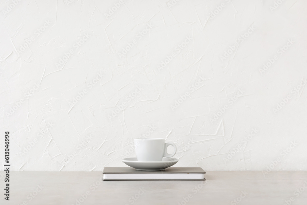 White cup with drink and notebook on neutral beige table, white concrete wall background with empty copy space. Minimalist brand template, coffee break, business lunch concept, home office workspace White cup with drink and notebook on neutral beige table, white concrete wall background with empty copy space. Minimalist brand template, coffee break, business lunch concept, home office workspace