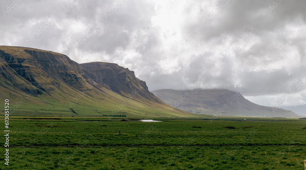 vue sur une montagne au loin avec une courbe au bas dans la vallée avec un champ de gazon vert en avant plan lors d'une journée nuageuse