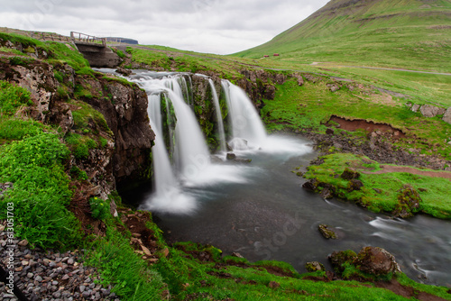 Fototapeta Naklejka Na Ścianę i Meble -  Vue sur une chute d'eau dans une rivière avec une vallée en arrière plan recouverte de gazon vert