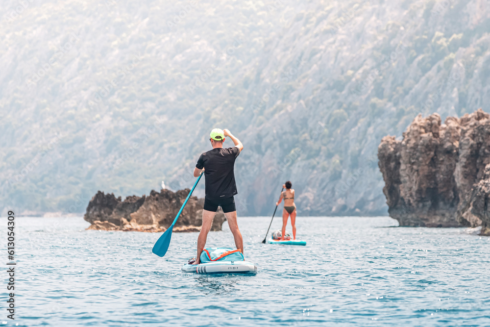 Naklejka premium Group or team with paddles swims on a SUP boards on the sea near scenic rocks. Healthy lifestyle and recreation concept