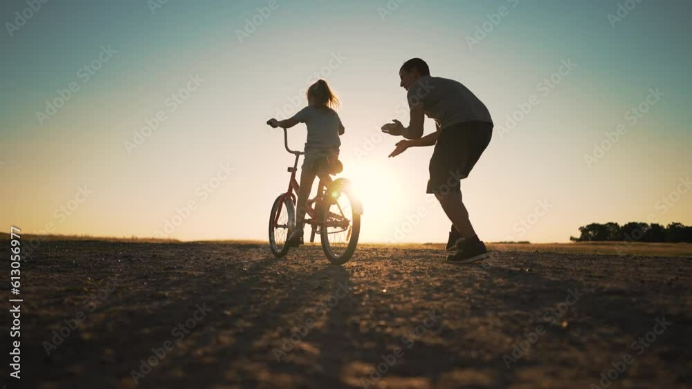 Happy family green park at sunset.Dad teaches daughter to rid bike in summer park.kid rides bicycle on green grass.Green energy.Dad teaches his daughter to ride bike for first time in park at sunset.