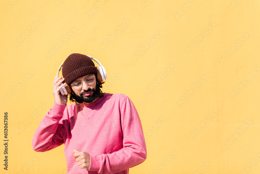 Φωτογραφία man dancing happy listening to music in his headphones with a yellow wall in the