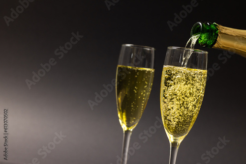 Close-up of champagne pouring in champagne flutes against black background, copy space