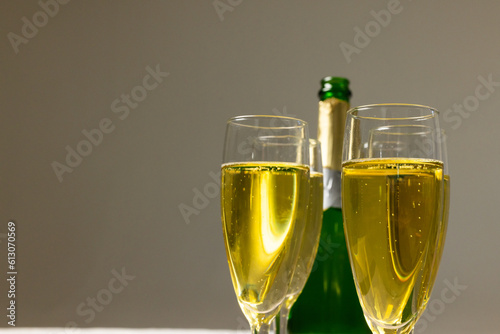 Close-up of champagne flutes with champagne bottle against gray background, copy space