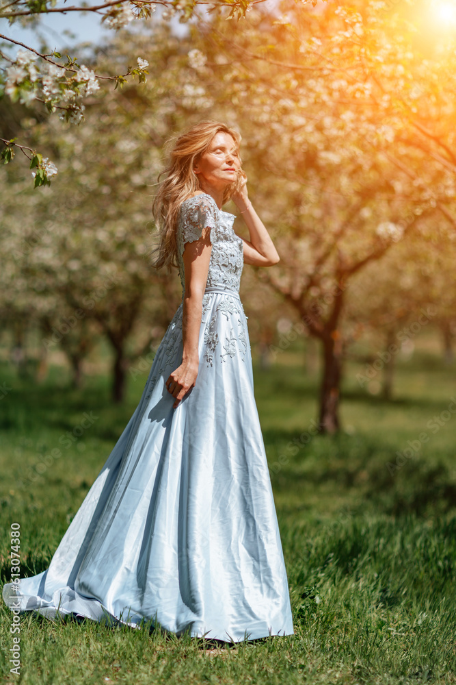 Blond garden. Portrait of a blonde in the park. Happy woman with long blond hair in a blue dress.
