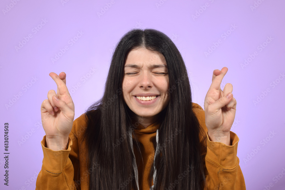 Young woman smiling while posing with fingers crossed for good luck Young woman smiling while posing with fingers crossed for good luck