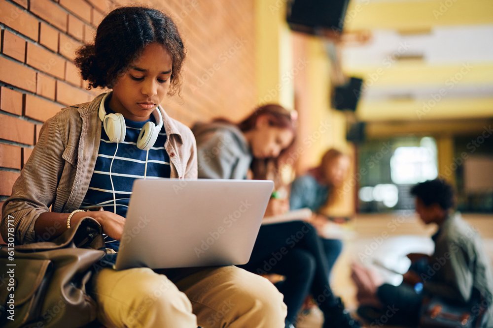 Black teenage girl e-learning on laptop in hallway at high school. Black teenage girl e-learning on laptop in hallway at high school.