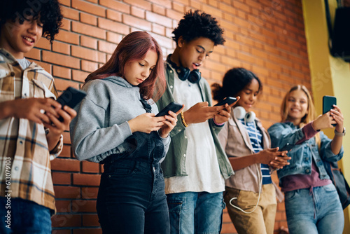 Multiracial group of teenagers using their cell phones at high school.