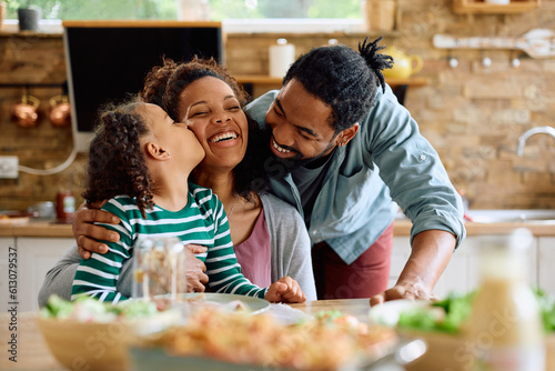Loving black family enjoys while having meal together at home. Daughter is kissing her mother.