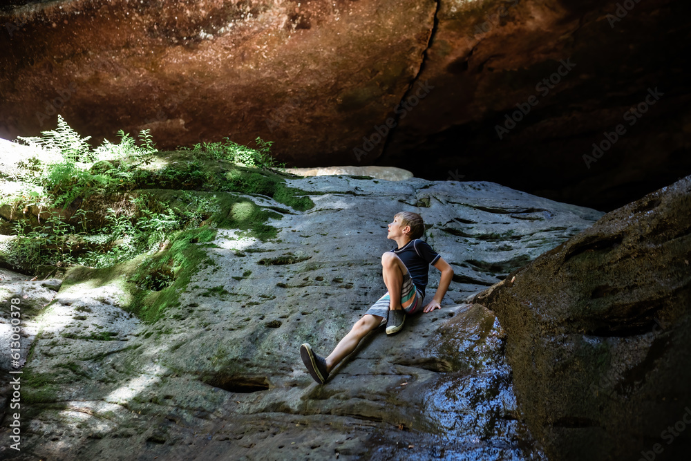 Child sitting on rocky cliff during summer hike looking up in wo Child sitting on rocky cliff during summer hike looking up in wo