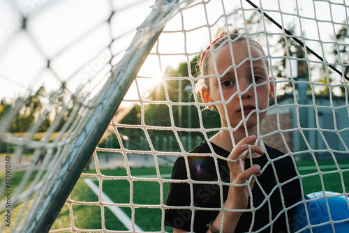 Girl stood goal holding a football looking through the goal net photo