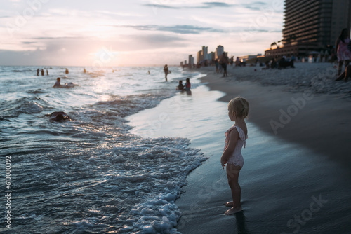 Child standing on shore watching tourists swim in ocean on summe photo