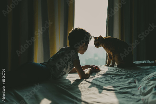 The boy and the cat lie on the bed and look at each other