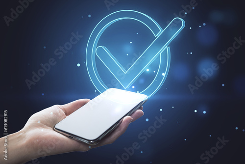 Photography Close up of female hand holding white cellphone with glowing blue polygonal checkmark on dark blurry background