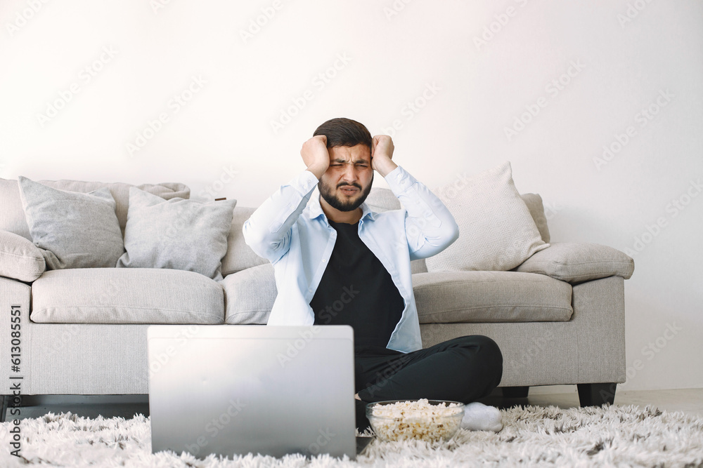 Brunette guy sitting on a floor and watching football on laptop Brunette guy sitting on a floor and watching football on laptop