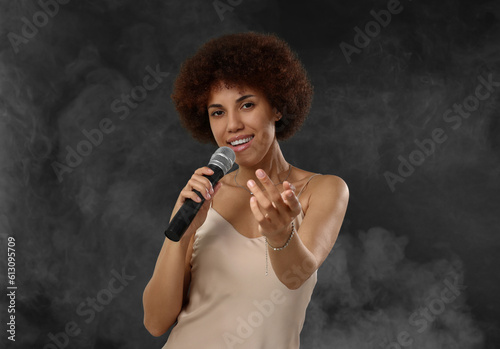 Curly young woman with microphone singing in smoke on black background