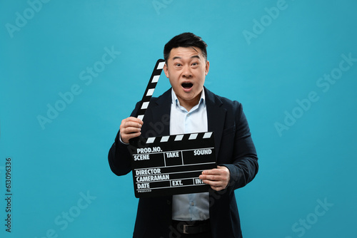 Emotional asian actor with clapperboard on light blue background. Film industry