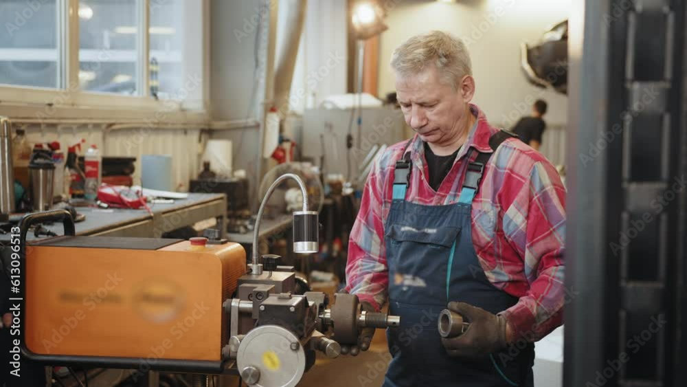 Mature middle age man mechanic in plaid shirt and uniform working with special equipment brake disc rotor resurfacing services in garage shop. Car brake repairing in garage Mature middle age man mechanic in plaid shirt and uniform working with special equipment brake disc rotor resurfacing services in garage shop. Car brake repairing in garage