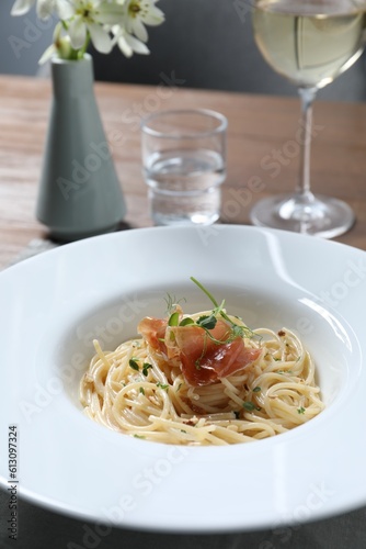 Tasty spaghetti with prosciutto and microgreens served on wooden table, closeup. Exquisite presentation of pasta dish