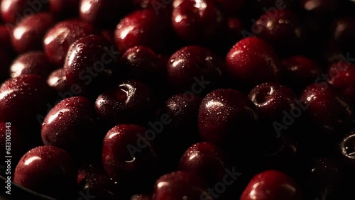 Red ripe cherries covered with water droplets, spinning on a black background. Wet sweet cherries rotate on a black plane