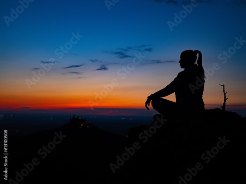 a girl in a lotus position sits on top of a mountain against the backdrop of sunset