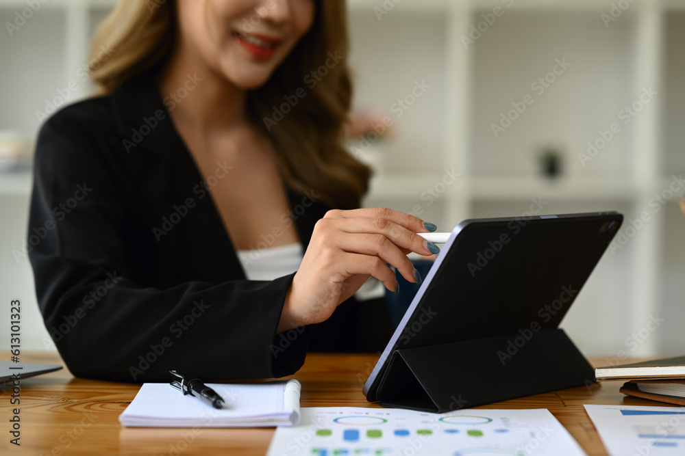 Smiling female analyst using digital tablet, checking marketing research results or statistics data at desk Smiling female analyst using digital tablet, checking marketing research results or statistics data at desk