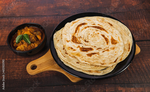 Kerala Parathas or Porotta Roti with red spicy chilly chicken. Barotta naan is a layered flatbread made from maida whole wheat flour. Indian food on a wooden table. photo