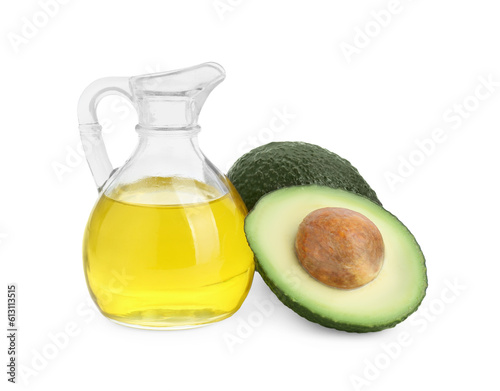 Jug of oil and fresh avocados on white background