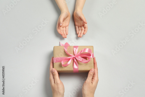 Mother giving gift box to her child on light gray background, top view