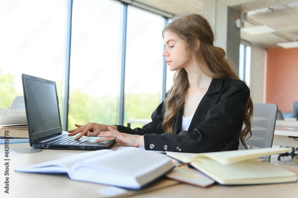 A beautiful caucasian female student is studying in college remotely. She is sitting with a laptop and a notepad and concentrated is watching a video conference lesson A beautiful caucasian female student is studying in college remotely. She is sitting with a laptop and a notepad and concentrated is watching a video conference lesson
