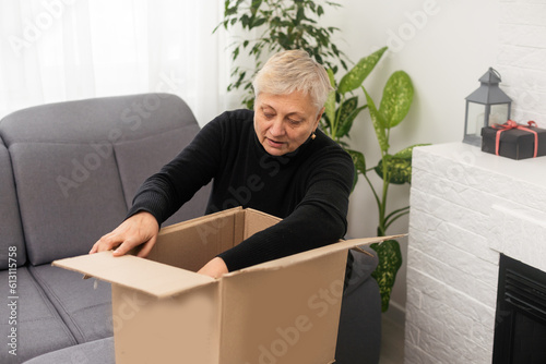 Elderly woman unpacking things in new house. Female hands opening cardboard box. Real estate, purchase, moving concept.