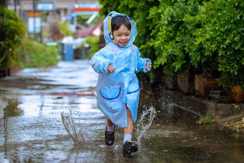 Asian boy wearing a raincoat outside the house. He is playing in the rain..