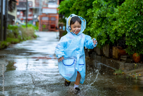 Fototapeta Naklejka Na Ścianę i Meble -  Asian boy wearing a raincoat outside the house. He is playing in the rain...