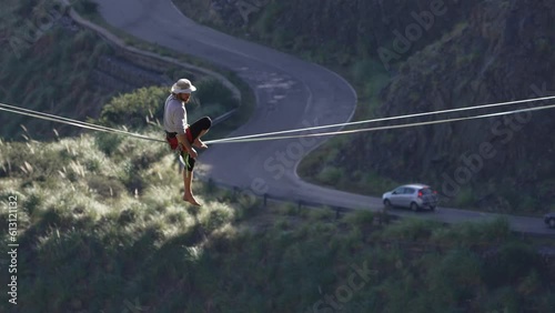 A man balancing on a highline contemplating a road with cars below. Slow motion. photo