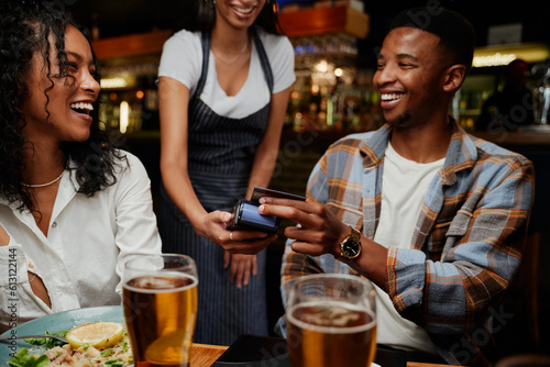Foto Happy multiracial friends in casual clothing paying waitress for dinner and drin