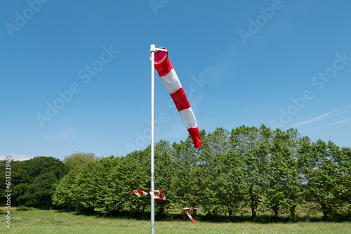 Cone giratório que indica a direção do vento colocado num locar de pouso para a prática de paraquedismo a meio a algumas árvores e verde relva
 photo