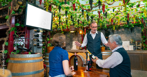 Professional senior man sommelier explaining and recommending wine to customer at wine shop or liquor store. Sommelier tasting wine in winery. Winery manufacturing industry and winemaker concept.