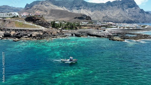 Wonderful aerial shot following a fishing boat in the turquoise waters of the port of Agaete on a sunny day and where the mountains and the coast can be seen. Canary Islands. photo