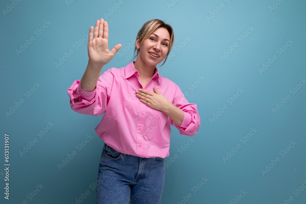young well-groomed pretty european blonde secretary woman dressed in a pink shirt shows her hand to the side of an advertisement offer on a studio background with copy space young well-groomed pretty european blonde secretary woman dressed in a pink shirt shows her hand to the side of an advertisement offer on a studio background with copy space