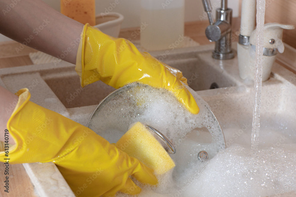 female hands in gloves wash dishes in soapy water in the sink in the