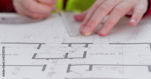 Schoolgirl imitates role of architect and makes line on flat layout with ruler. Little girl draws circle with protractor and pencils on drawing of apartment closeup