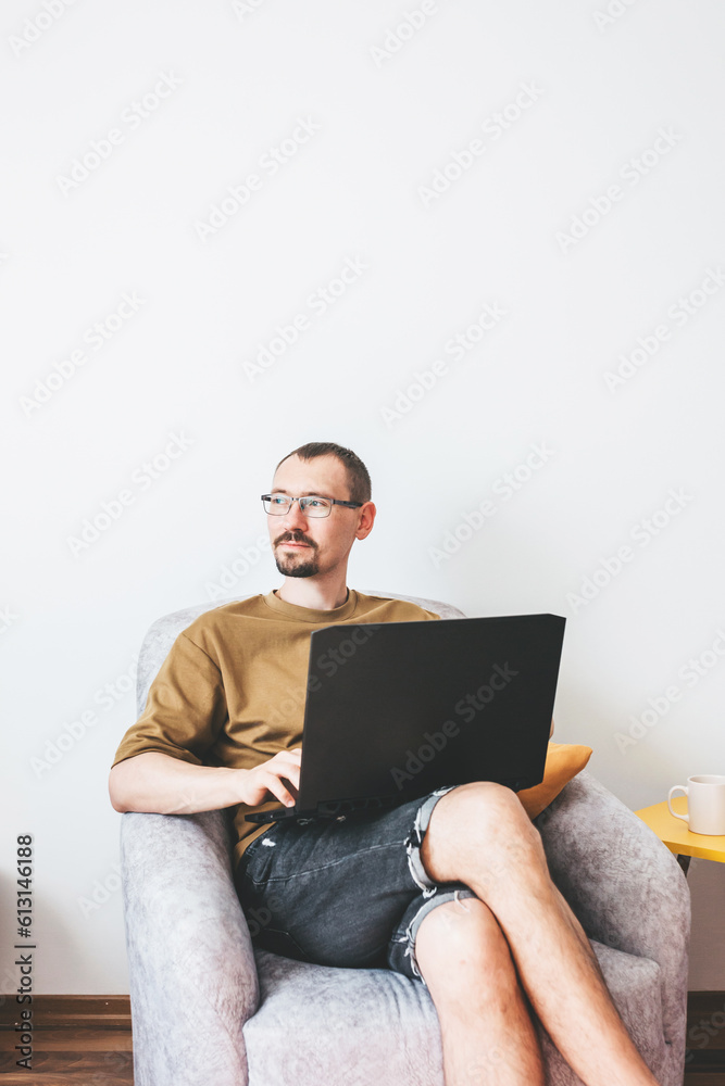 A young man using a laptop for remote work from home, conducts a video call, engages in e-mail, communicates online, sends emails, develops software while sitting at home on the couch. A young man using a laptop for remote work from home, conducts a video call, engages in e-mail, communicates online, sends emails, develops software while sitting at home on the couch.