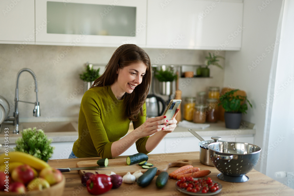 Young woman text messaging while cutting vegetables on cutting board in the kitchen