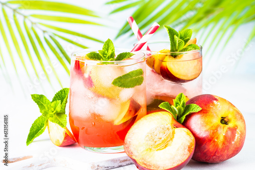 Peach cocktail, iced peach tea, fruit drink at tropical background with palm leaves. Summer drink.