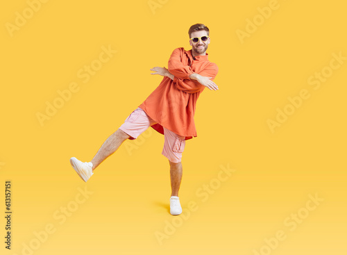 Full body photo of cool funny young guy with unshaven beard dancing wearing bright summer casual clothes and white sneakers isolated on a yellow background. Man having fun in studio.